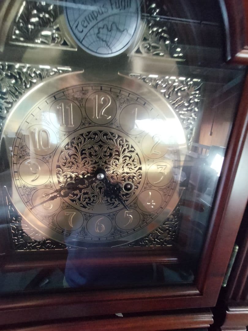 装飾的な文字盤と振り子を持つダークウッドの柱時計